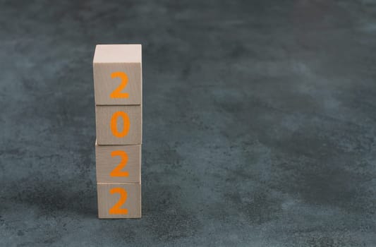 The year 2022 is standing on wooden cubes, dark background, empty copy space