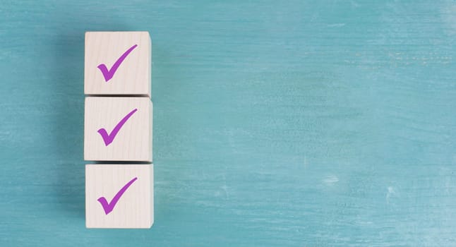 Three wooden cubes with purple checkmarks, blue background, copy space for text