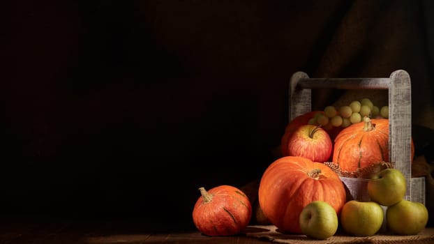 Autumn still life with pumpkins, apples, grape and pears  in a wooden box on dark background with sunlight. Copy space. Autumn harvest, Happy Thanksgiving