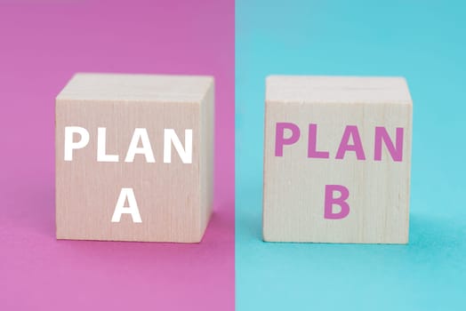 Plan A and B standing on wooden cubes, pink and blue colored background, options of possibilities