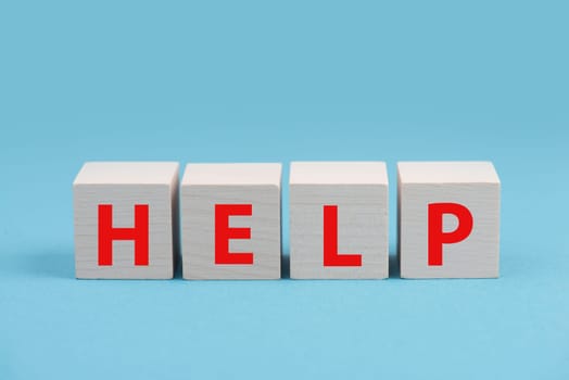The word help is standing in red letters on wooden cubes, blue colored background