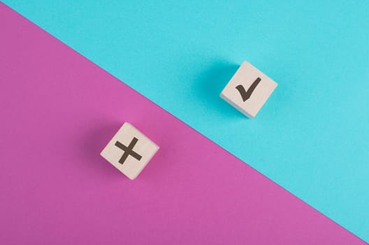 Wooden cubes with check mark and cross on a pink and blue colored vibrant background, minimalism