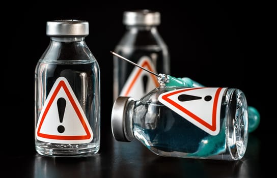 Vaccine bottles with red triangle exclamation mark sign on label, black background.