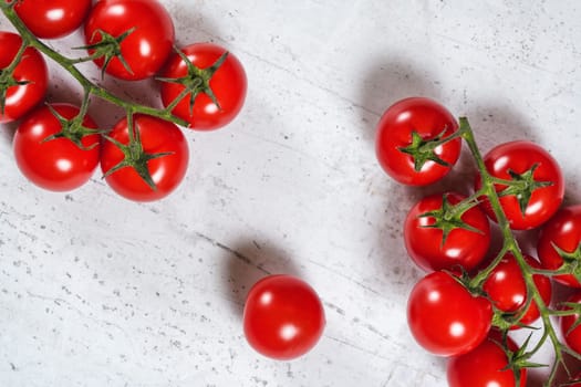 Vibrant small red tomatoes with green vines on white stone like board, view from above.