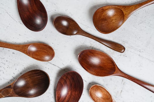 Small spoons made of dark wood, on white working board, view from above.