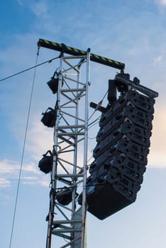 Line array speaker system hanging from pole during daylight performance. Sunset blue sky background