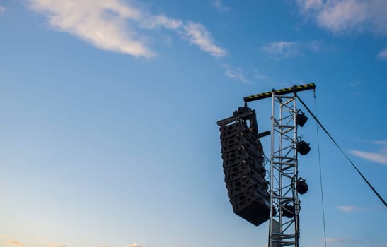 Line array speaker system hanging from pole during daylight performance. Sunset blue sky background