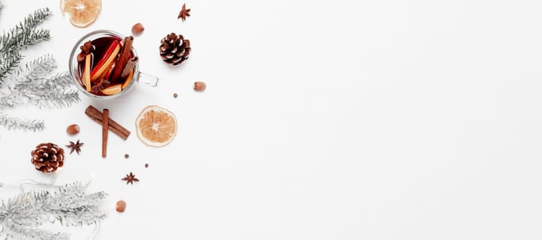 Christmas banner flat lay on white gray background with glass cup or mug of Mulled Wine, present red gift box, decorations, cinnamon, orange, apple, various spices, fir, cone, anise. Conceptual photo