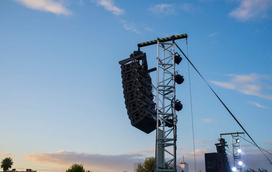 Line array speaker system hanging from pole during daylight performance. Sunset blue sky background