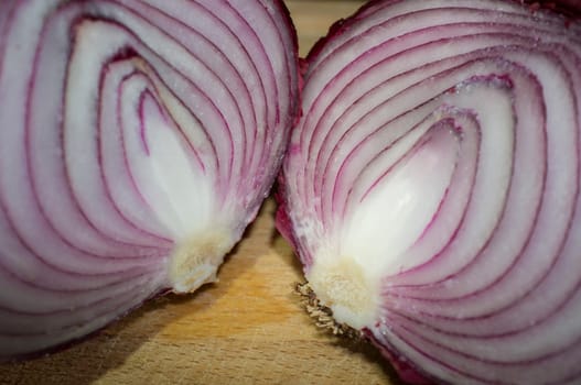 Cross sections of raw red onions. Closeup over wooden cutting board