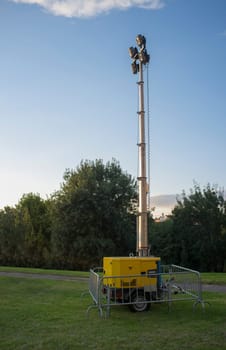 Moble fuel consumption light tower over grass during daylight performance. Sunset blue sky background