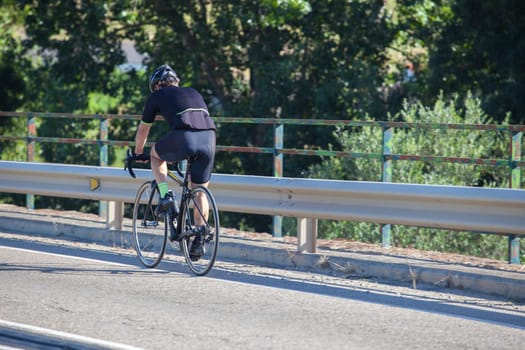 Mature biker crossing river bridge on local road. Road biking by Extremadura, Spain