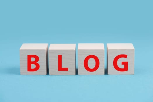 The word blog is standing in red colored letters on wooden cubes, blue background