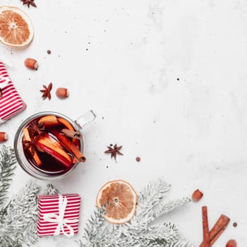 Christmas flat lay top view on gray concrete background with mulled wine glass cup or mug, red gift boxes, decorations, cinnamon sticks, hazelnut, orange, apple, various spices. Christmas time photo