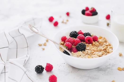 Morning healthy breakfast, white bowl full with granola, muesli, raspberry, blackberry on gray concrete table. Healthy eating, eco, bio food concept. Fresh tasty meal on grey background. Quality photo