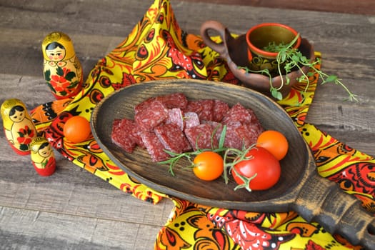 Dry salami on rustic black table with yellow khokhloma decoration