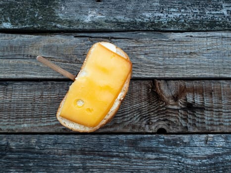 Hard cheese sandwich and a cup of coffee on a wooden table. Hard cheese. Butter. White bread. Cardboard coffee cup. Wooden table. Morning breakfast. Food intake. Street Cafe.