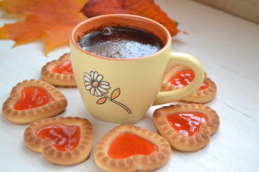 black coffee in orange cup with cookies hearts, autumn maple leaf on white table, bright image