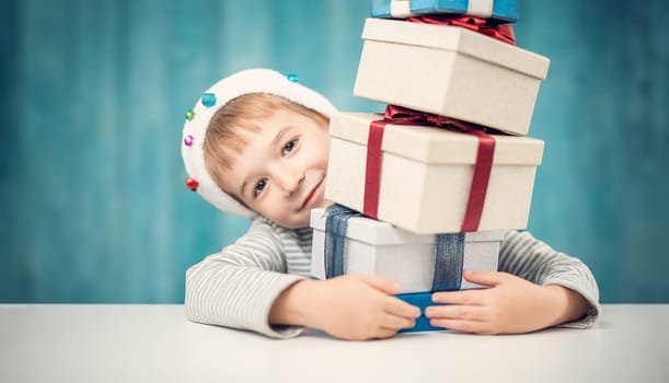 Cute child sitting at the table with stack of giftboxes. Concept of Christmas and New Year celebrating.