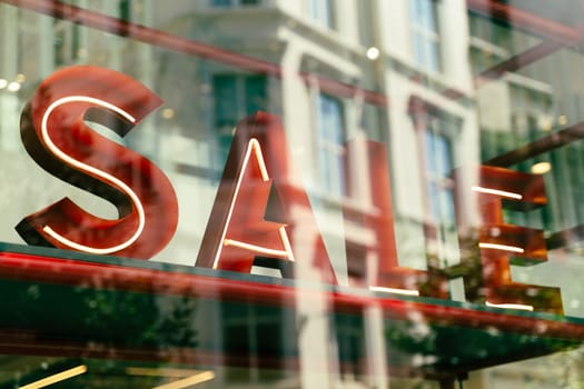 perspective closeup view of sale signage sign with volumetric neon letters in mall shop window with reflections on glass