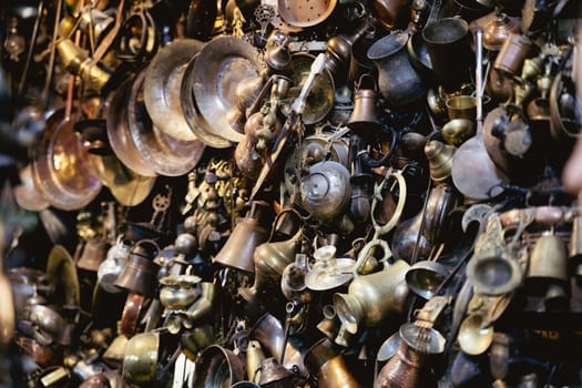 perspective view closeup of many different metallic antique pots plates and bowls of different sizes and shapes hanging on a wall in a shop