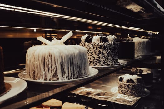 perspective view closeup of rows of assorted chocolate birthday cakes lined up on the shelf in the dark window of a sweet shop
