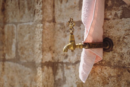 closeup of vintage bronze water faucet with decorated tap and bath towel next to a Muslim mosque with stone background