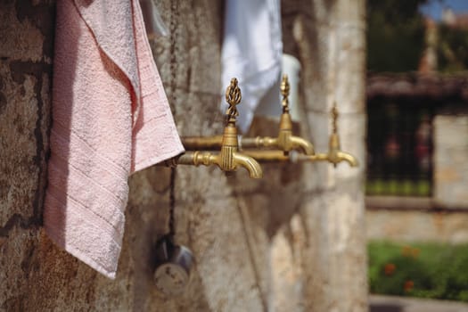 closeup of vintage bronze water faucet with decorated tap and bath towel next to a Muslim mosque with stone background