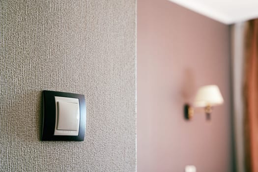 front view closeup of white light plastic switch socket on textured wall with home interior in the background