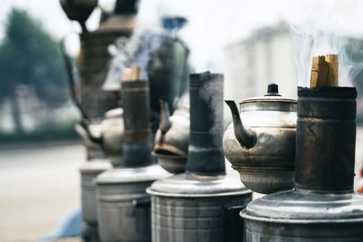 closeup perspective view row of traditional Turkish tea metallic samovars and kettles warmed outside with burning wood