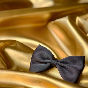 Black bow tie on draped golden satin