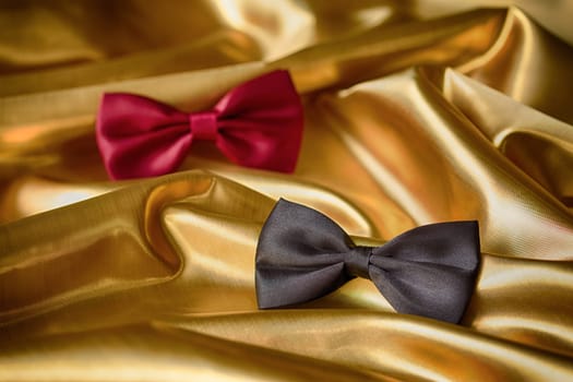 Red and black bow ties on draped golden satin