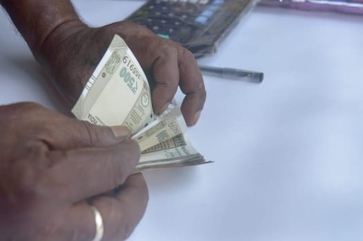 Senior aged Man hand counting Indian rupee note on table. High angle view. Close up.
