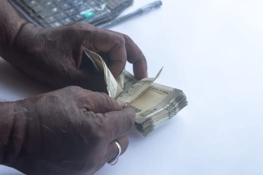 Black Man hand counting five hundred Indian rupee note on table. High angle view. Close up. White background.