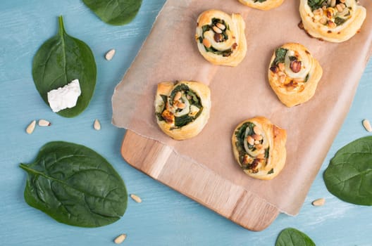 Puff pastry with spinach and feta cheese, rolled up to spirals, fresh from the oven, blue background
