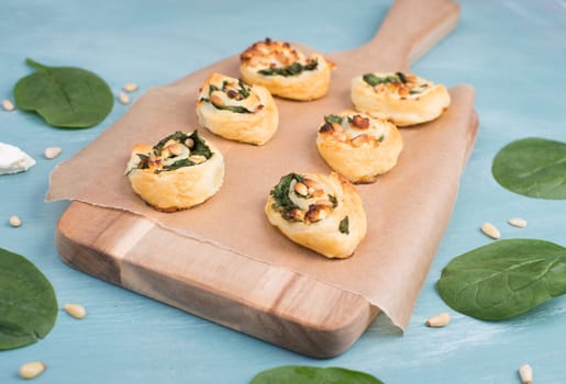 Puff pastry with spinach and feta cheese, rolled up to spirals, fresh from the oven, blue background
