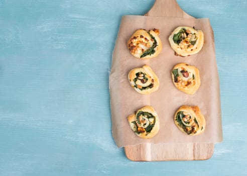 Puff pastry with spinach and feta cheese, rolled up to spirals, fresh from the oven, blue background