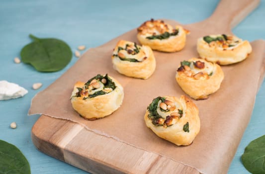 Puff pastry with spinach and feta cheese, rolled up to spirals, fresh from the oven, blue background