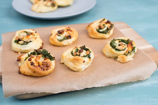 Puff pastry with spinach and feta cheese, rolled up to spirals, fresh from the oven, blue background