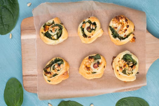 Puff pastry with spinach and feta cheese, rolled up to spirals, fresh from the oven, blue background