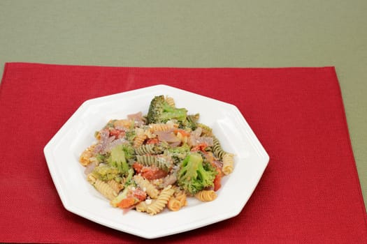 Parmesan cheese topped tri-color vegetable rotini pasta with broccoli, tomato and onions on a plate. Cooked vegetable rotini pasta with mixed vegetables of broccoli, tomatoes and onions with cheese.