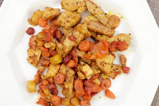 Lunch of cooked chicken meat, orange, purple and yellow carrots, and tomatoes with herbs on an octagon plate. Healthy nutritious meal of chicken with vegetables and herbs on a plate close-up.