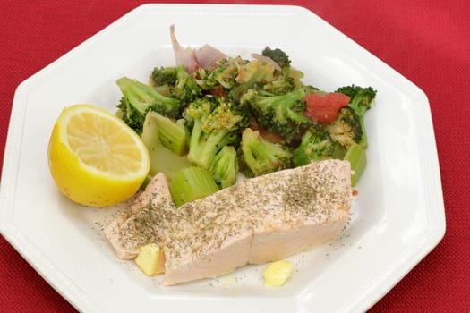 Farmed salmon fillet with dill butter and mixed vegetables on a white plate close-up. Ready-to-eat salmon fish farm raised with seasoned vegetables dinner with dill, butter and a variety of vegetables