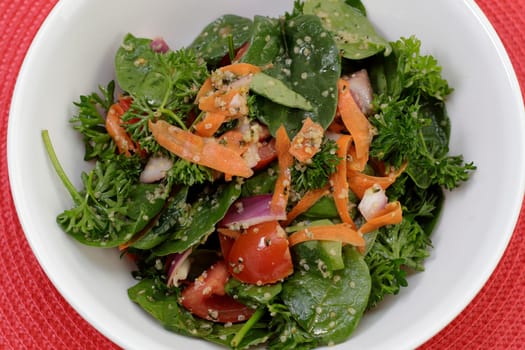 Nutritious spinach greens and parsley salad with mixed vegetables, shelled hemp hearts and seasonings. Bowl of a very nutritious nutrient dense salad of spinach and vegetables, simple salad dressing..