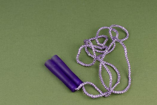 Exercise equipment jump rope with purple grips and purple and white rope exercise equipment on a green cloth. Close-up of purple and white skipping jump rope with purple grips on a green background.