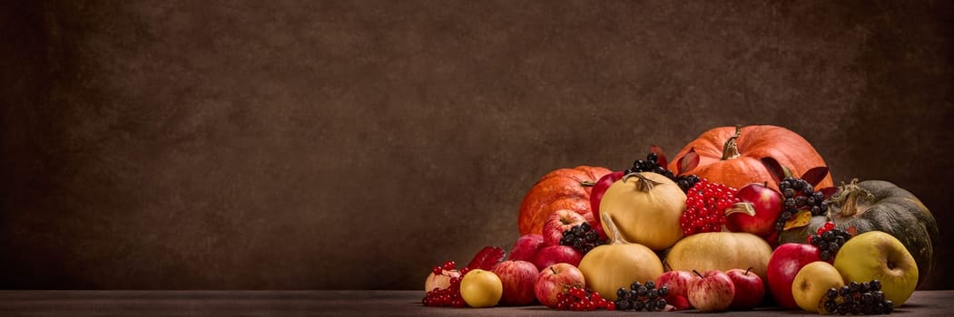 Thanksgiving extra wide panorama background. Festive still life with pumpkins, berries, autumn leaves and apples on dark brown background with copy space. Happy Thanksgiving day, autumn harvest, Halloween.