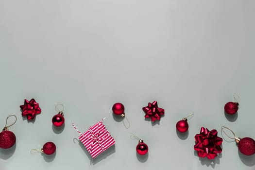 Gray background with pink Christmas gift box present, small red Christmas balls or sphere toys, ribbon bows for fir tree, other decorations. Christmas sales, shopping or greeting card or invitation