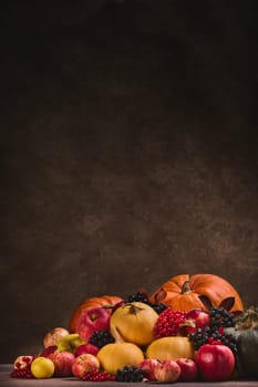 Thanksgiving background. Festive still life with pumpkins, berries, autumn leaves and apples on dark brown background with copy space. Happy Thanksgiving  day, autumn harvest, Halloween. Vertical orientation