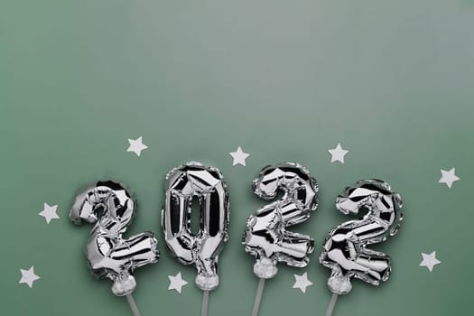 New Year 2022 or Christmas green background flat lay. Top view on 2022 balloon silver or metallic numbers on sticks with stars. Invitation or greeting card concept. Festive mood. High quality photo
