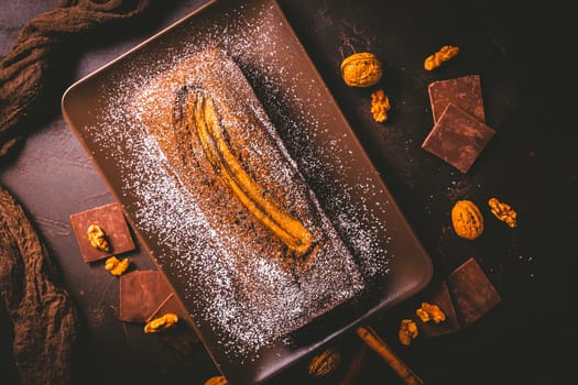Homemade vegan banana bread or cake with nuts, chocolate and cinnamon on brown background